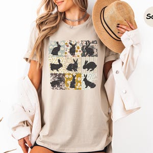 Puede incluir: Camiseta beige con una cuadr&iacute;cula de nueve siluetas de conejos sobre fondos florales y estampados. Los conejos est&aacute;n en varias poses y colores. La camiseta es de color neutro y el dise&ntilde;o tiene una est&eacute;tica vintage.