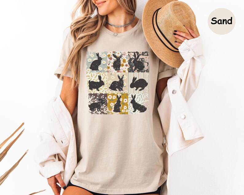 Puede incluir: Camiseta beige con una cuadr&iacute;cula de nueve siluetas de conejos sobre fondos florales y estampados. Los conejos est&aacute;n en varias poses y colores. La camiseta es de color neutro y el dise&ntilde;o tiene una est&eacute;tica vintage.