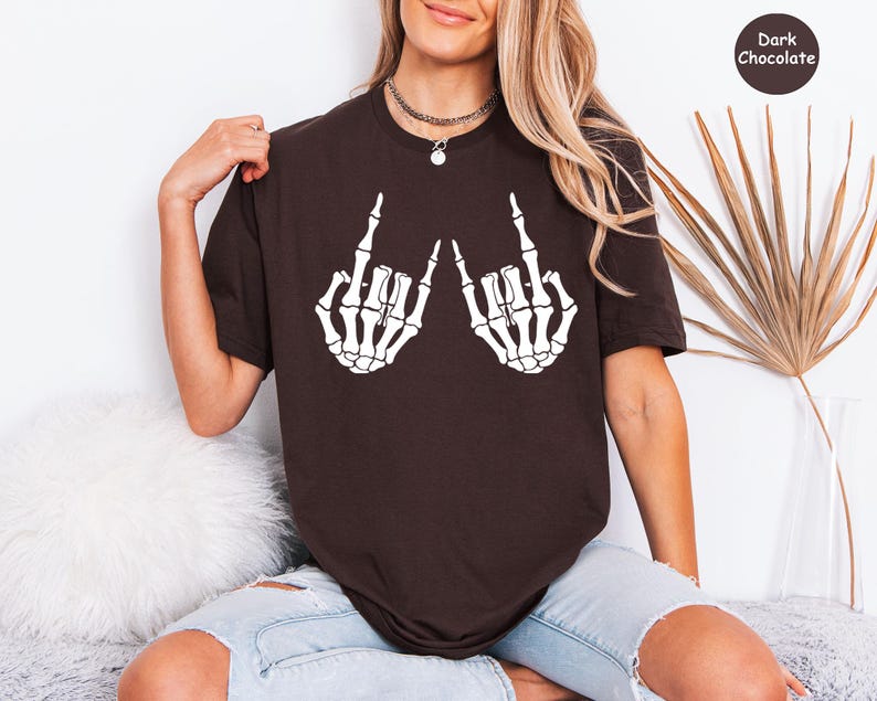 May include: A dark chocolate brown short-sleeve t-shirt featuring a white graphic print of two skeleton hands making the rock and roll hand sign. The upper right corner of the image contains a small circular badge with the text Dark Chocolate.