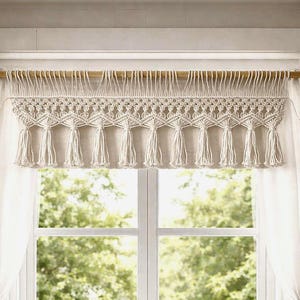 May include: A kitchen window with a macrame valance, white curtains, and a farmhouse sink. The window overlooks a lush green outdoor scene. The kitchen features a stainless steel faucet, wooden cutting boards, and potted plants.