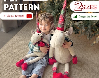 May include: A child holds two plush reindeer dolls. The dolls have cream-colored bodies, red accents, and plaid hats. The image includes text that says "PDF PATTERN" and "2 SIZES".