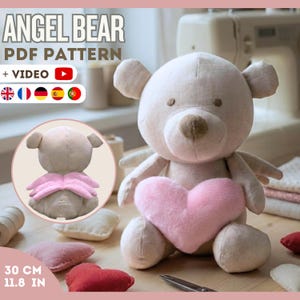 May include: A beige plush bear with a pink heart, wings, and brown accents. The bear is approximately 11.8 inches tall. The image includes the text "ANGEL BEAR PDF PATTERN + VIDEO".