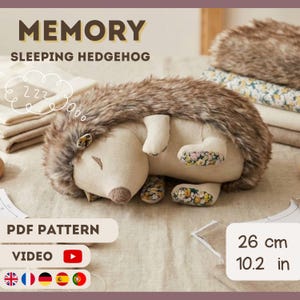 May include: A plush sleeping hedgehog toy with a light brown and beige color scheme. The hedgehog has a soft, textured back and floral patterned feet. The image includes the text "MEMORY SLEEPING HEDGEHOG", and the dimensions are 10.2 inches.
