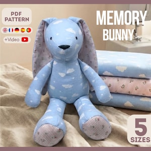 May include: A plush blue bunny with white cloud patterns, labeled "Memory Bunny." The bunny has pink floral fabric on the inner ears and feet. The image also shows a stack of fabric and the text "5 SIZES."
