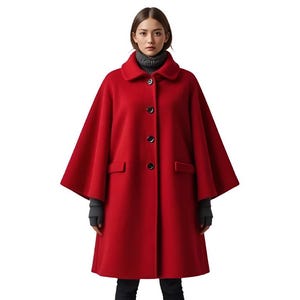 Op de afbeelding: Een felrode capejas met een klassieke kraag en drie zwarte knopen. De jas heeft een uitlopend silhouet en twee voorzakken. Het model draagt een grijze coltrui en zwarte handschoenen.