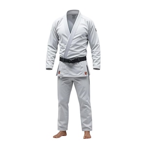 Puede incluir: Un uniforme de Jiu-Jitsu gris claro, que incluye una chaqueta con solapa y pantalones. El uniforme tiene un cinturón negro y se muestra sobre un fondo blanco. La chaqueta tiene un cuello reforzado y los pantalones tienen cintura con cordón.