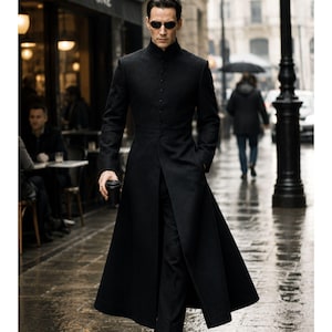 May include: A black, long coat with a high collar and button-down front. The coat is worn with black pants and sunglasses. The person is holding a black coffee cup and walking on a wet, cobblestone street.