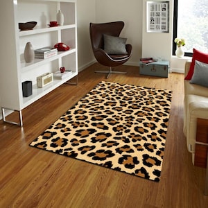 May include: Rectangular area rug with a leopard print pattern. The rug features a tan background with brown and black spots. The rug is placed on a hardwood floor in a living room setting.