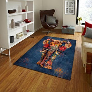 May include: A rectangular blue area rug featuring a colorful elephant design. The elephant is adorned with floral patterns in shades of red, orange, and yellow. The rug is placed on a wooden floor.
