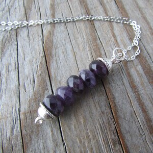 May include: A silver chain necklace with a pendant made of five faceted amethyst beads. The beads are strung on a silver wire and the pendant is attached to the chain with a silver clasp.