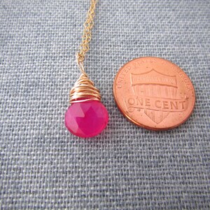 May include: A pink gemstone pendant necklace with a gold wire wrap. The pendant is about the size of a US penny.