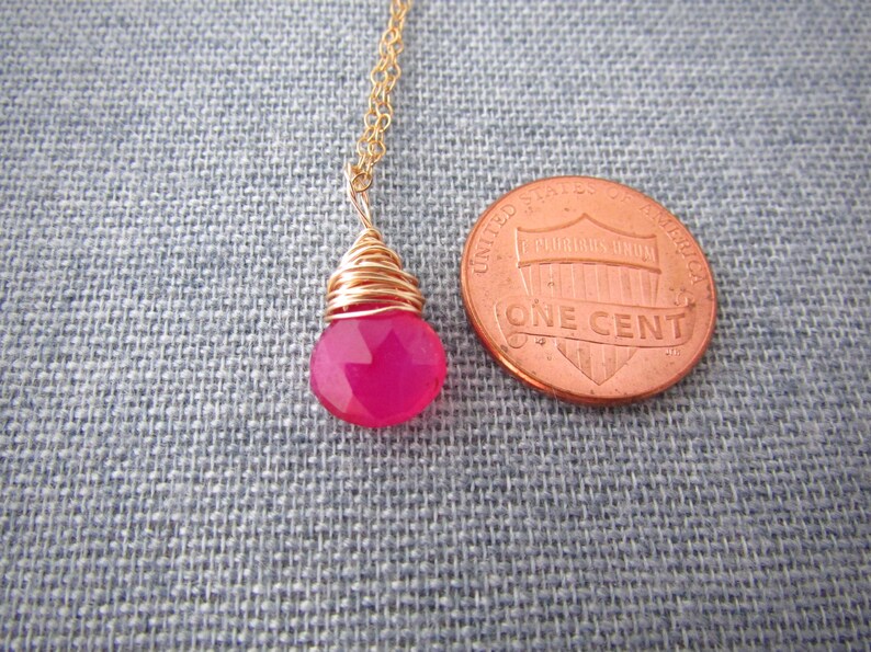 May include: A pink gemstone pendant necklace with a gold wire wrap. The pendant is about the size of a US penny.