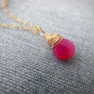 May include: A gold chain necklace with a pink gemstone pendant wrapped in gold wire.