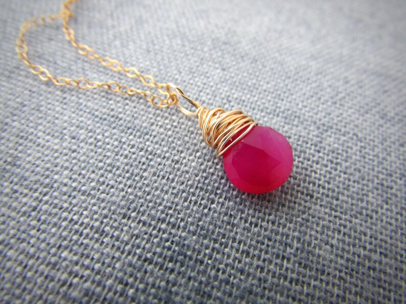 May include: A gold chain necklace with a pink gemstone pendant wrapped in gold wire.