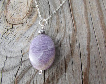 May include: A silver chain necklace with a purple and white oval pendant. The pendant is made of a natural stone and has a silver bead at the top.