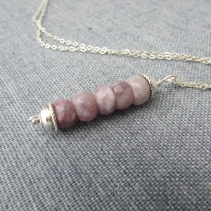May include: A silver chain necklace with a pendant made of five round, light purple and white gemstone beads. The beads are strung on a silver wire and have a silver clasp.