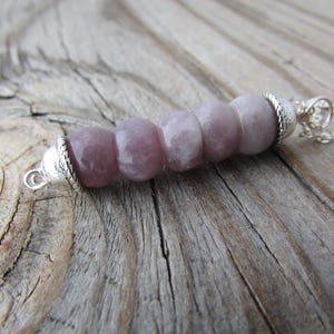 May include: A silver chain necklace with a pendant made of five light purple and white gemstone beads.
