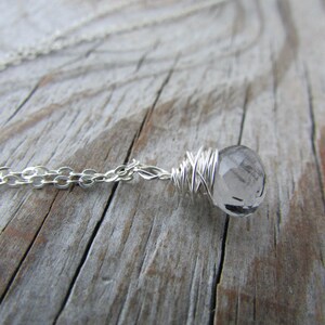 May include: A silver chain necklace with a clear quartz crystal wrapped in silver wire.