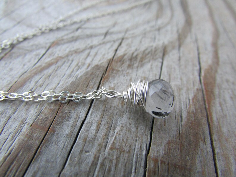 May include: A silver chain necklace with a clear quartz crystal wrapped in silver wire.