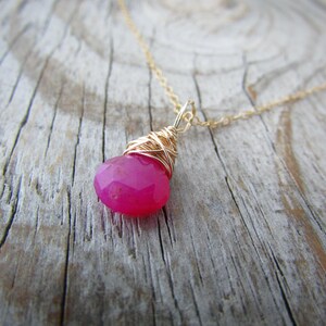 May include: A gold chain necklace with a pink gemstone pendant wrapped in gold wire.