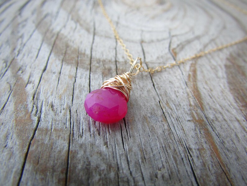 May include: A gold chain necklace with a pink gemstone pendant wrapped in gold wire.