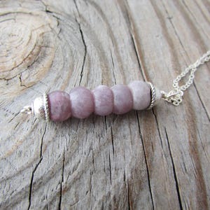 May include: A silver chain necklace with a pendant made of five round, light purple beads. The beads are strung together on a silver wire and have a silver clasp.