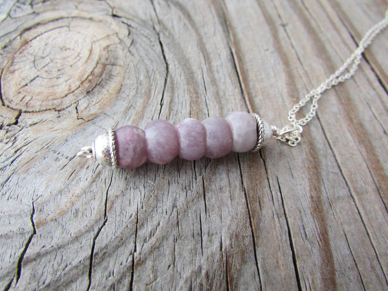 May include: A silver chain necklace with a pendant made of five round, light purple beads. The beads are strung together on a silver wire and have a silver clasp.