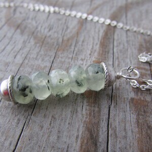 May include: A silver chain necklace with a pendant made of faceted green and black stones. The pendant is attached to the chain with a silver clasp.
