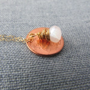 May include: A gold chain necklace with a white gemstone pendant wrapped in gold wire. The pendant is about the size of a US penny.