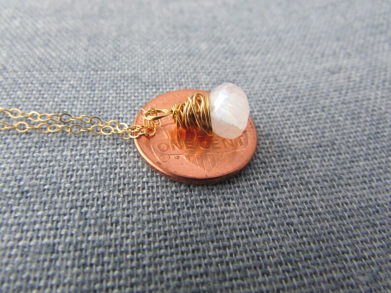 May include: A gold chain necklace with a white gemstone pendant wrapped in gold wire. The pendant is about the size of a US penny.