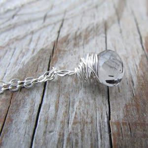 May include: A silver chain necklace with a clear quartz crystal wrapped in silver wire.