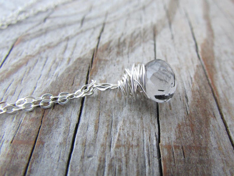 May include: A silver chain necklace with a clear quartz crystal wrapped in silver wire.
