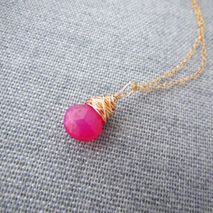 May include: A gold chain necklace with a pink gemstone pendant wrapped in gold wire.