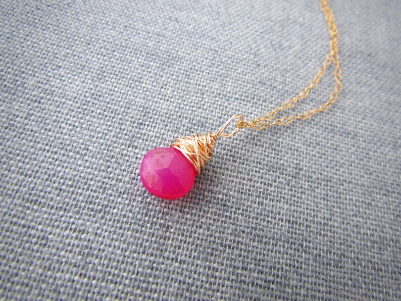 May include: A gold chain necklace with a pink gemstone pendant wrapped in gold wire.