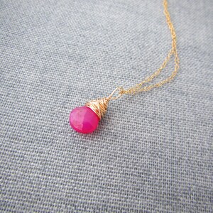 May include: A delicate gold chain necklace with a pink gemstone pendant wrapped in gold wire.