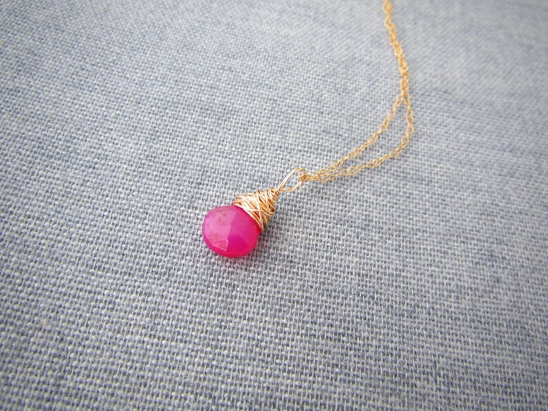 May include: A delicate gold chain necklace with a pink gemstone pendant wrapped in gold wire.