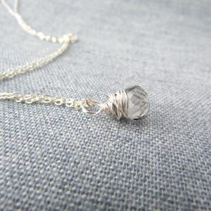 May include: A silver chain necklace with a clear quartz crystal pendant wrapped in silver wire.