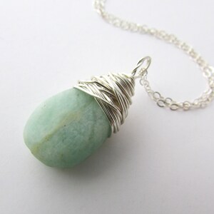 Pu&ograve; includere: Una collana con catena d'argento con un ciondolo di pietra preziosa verde chiaro avvolto in filo d'argento.