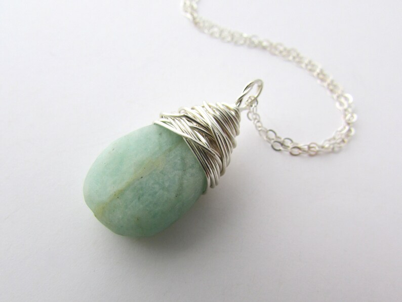 Pu&ograve; includere: Una collana con catena d'argento con un ciondolo di pietra preziosa verde chiaro avvolto in filo d'argento.
