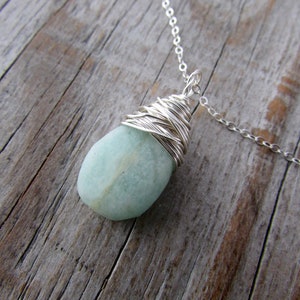 Pu&ograve; includere: Una collana con catena d'argento con un ciondolo di pietra preziosa blu chiaro avvolto in filo d'argento.