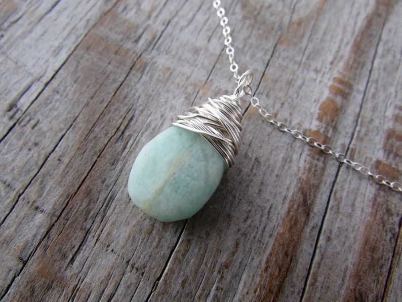 Pu&ograve; includere: Una collana con catena d'argento con un ciondolo di pietra preziosa blu chiaro avvolto in filo d'argento.