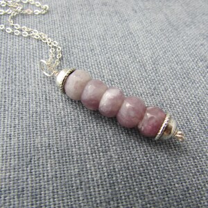 May include: A silver chain necklace with a pendant made of six round, light purple and white stones with silver accents.
