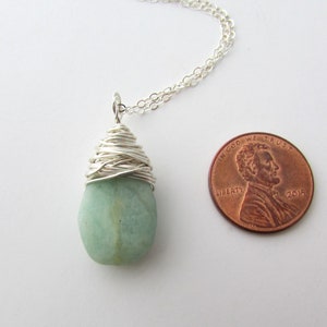 Pu&ograve; includere: Una collana con catena d'argento con un ciondolo di pietra preziosa verde chiaro avvolto in filo d'argento. Il ciondolo &egrave; circa delle dimensioni di una moneta da un centesimo di dollaro.
