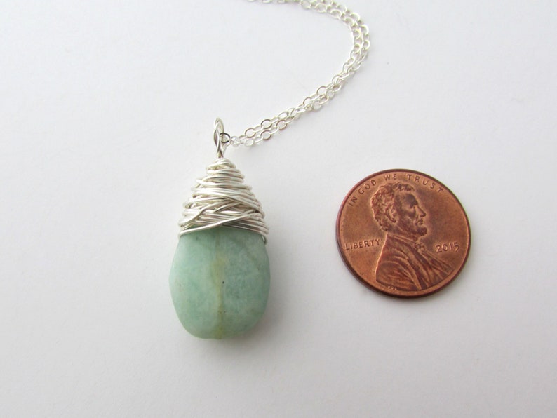 Pu&ograve; includere: Una collana con catena d'argento con un ciondolo di pietra preziosa verde chiaro avvolto in filo d'argento. Il ciondolo &egrave; circa delle dimensioni di una moneta da un centesimo di dollaro.