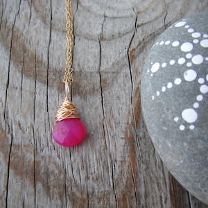May include: A gold chain necklace with a pink gemstone pendant wrapped in gold wire.