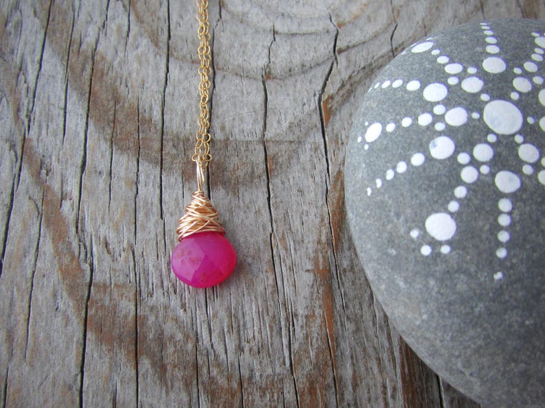 May include: A gold chain necklace with a pink gemstone pendant wrapped in gold wire.