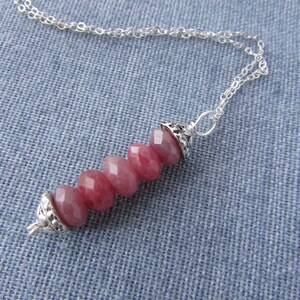 May include: A silver chain necklace with a pendant made of pink and red gemstone beads. The beads are faceted and have a smooth, polished finish. The pendant is attached to the chain with a silver clasp.