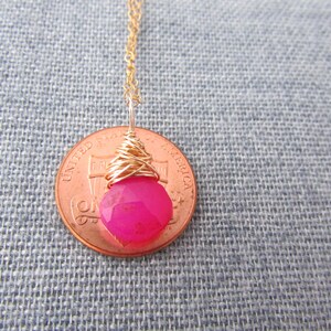 May include: A pink gemstone pendant necklace with gold wire wrapping. The pendant is about the size of a US penny.