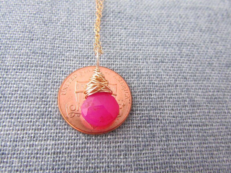 May include: A pink gemstone pendant necklace with gold wire wrapping. The pendant is about the size of a US penny.