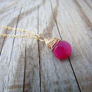May include: A gold chain necklace with a pink gemstone pendant wrapped in gold wire.